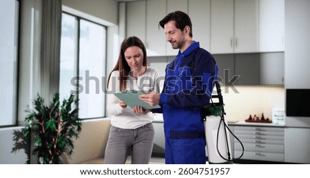 Pest control worker explains invoice to woman in kitchen at home.