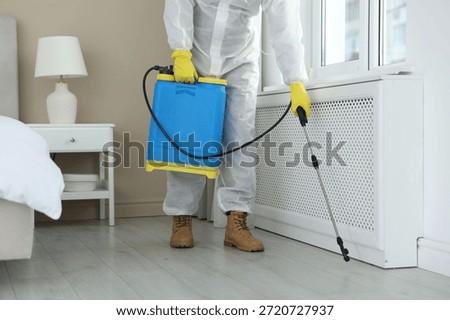 Pest control worker in protective suit spraying insecticide indoors, closeup