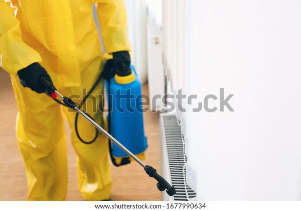 Pest control worker in protective\
suit spraying pesticide indoors, closeup. Space for\
text