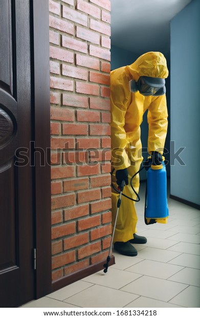 Pest control worker in protective suit spraying\
pesticide indoors