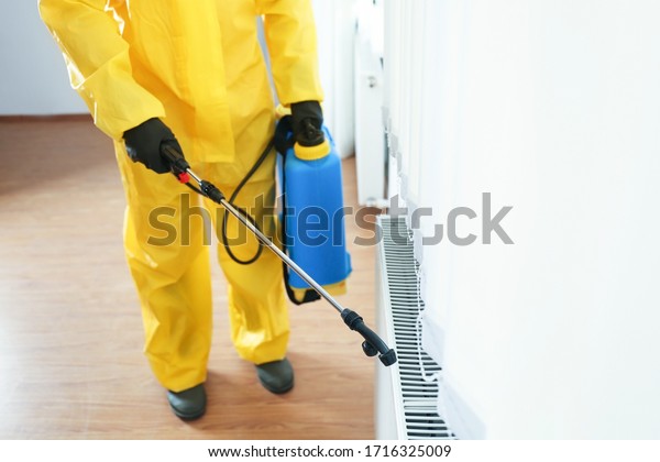 Pest control worker in protective\
suit spraying pesticide indoors, closeup. Space for\
text