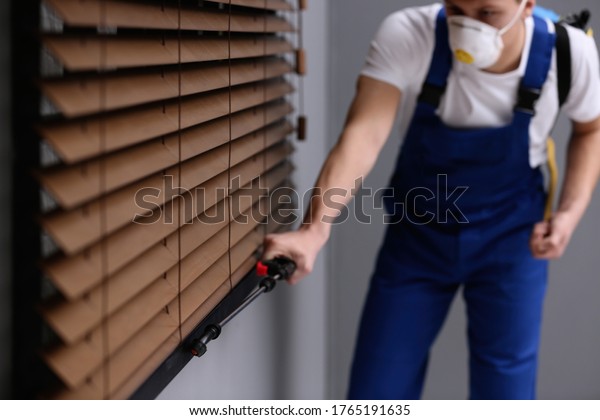 Pest control worker spraying pesticide near\
window in room, focus on\
sprayer