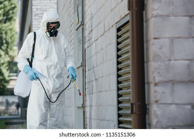 Pest Control Worker Spraying Pesticides With Sprayer On Building Wall On Street