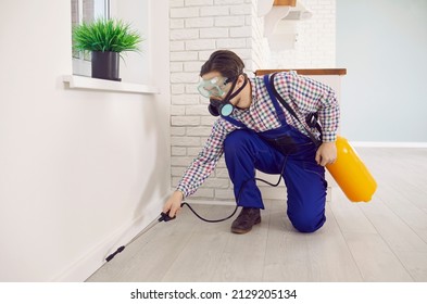 Pest control worker spraying poisonous liquid inside the house infested by ants or wood eating termites. Young male exterminator wearing protective mask and workwear uniform disinsecting a modern home