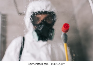 pest control worker standing in respirator in bathroom with sprayer