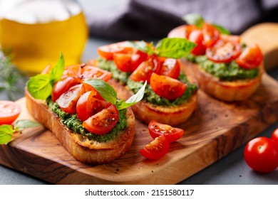 Pesto Bruschetta, Crostini With Tomato, Fresh Basil On Wooden Cutting, Serving Board. Grey Background. Close Up.