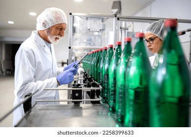 PET packaging bottling plant and workers in white coat controlling water production. - Shutterstock ID 2258399633
