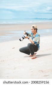 Petchaburi,Thailand -July 10,2021 :Candid Of Young Attractive Asian Man Hold Camera Taking Photo In Sea View Background. Happy Asian Hipster Male Photographer In Youth Freedom Culture Lifestyle Travel