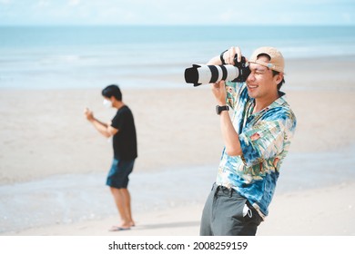 Petchaburi,Thailand -July 10,2021 :Candid Of Young Attractive Asian Man Hold Camera Taking Photo In Sea View Background. Happy Asian Hipster Male Photographer In Youth Freedom Culture Lifestyle Travel