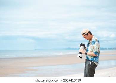 Petchaburi,Thailand -July 10,2021 :Candid Of Young Attractive Asian Man Hold Camera Taking Photo In Sea View Background. Happy Asian Hipster Male Photographer In Youth Freedom Culture Lifestyle Travel