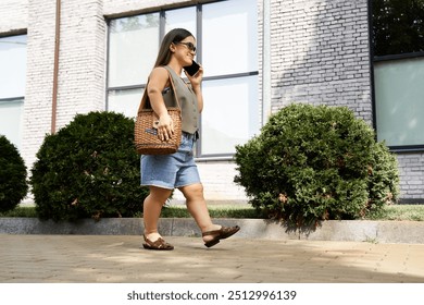 A petite brunette woman strolls along a tree-lined path, engaged in a lively phone conversation, radiating joy. - Powered by Shutterstock