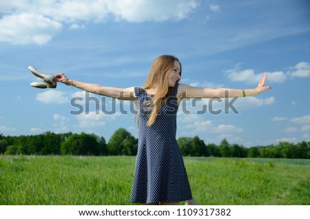 Petite woman walking in the meadow, bare feet and shoes in her hand. Female model enjoys nature and freedom with open arms.