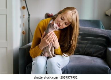 Petrenthood. Woman Enjoying Time With Gray Bald Sphynx Kitty. Sitting On Couch In Living Room. Petting And Giving Care To Sweet Animal. Blond Owner Pampering Cat. Petriarchy Concept