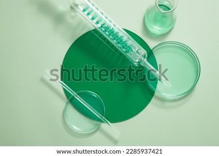 Petri dishes, test tube with spiral pipe and an erlenmeyer flask filled with green fluid. Vacant space on the plastic board to show your product