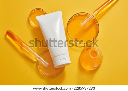 Petri dishes, test tubes and an erlenmeyer flask of orange liquid displayed with a white tube. Minimalism brand packaging mockup. Laboratory experience and research