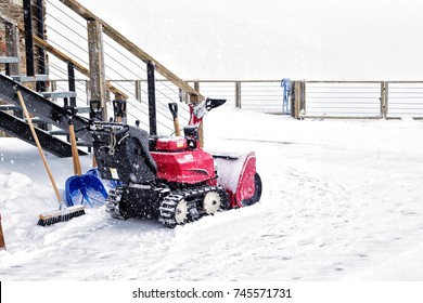 The petrol snow blower in snowfall. The portable snowplow and a shovel in the yard at a ladder, a heavy snowfall, snow on the cleared-away path - Powered by Shutterstock