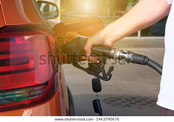 Petrol station pump. Pumping gasoline fuel in\
orange car at a gas station. To fill orange car with fuel in petrol\
station. Sunlight.
