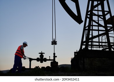 Petroleum operator in work vest using oil pump rocker-machine to extract crude oil from well. Male worker operating petroleum pump jack while working in oil field. Concept of oil extraction.