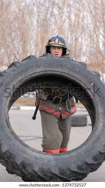 PETROPAVLOVSK CITY, KAMCHATKA PENINSULA,\
RUSSIA - APR 19, 2019: Strong firefighter-rescuer Emercom of Russia\
tilting big tire from truck. Firefighters and rescuers\
(fire-fighting) sport\
competitions.