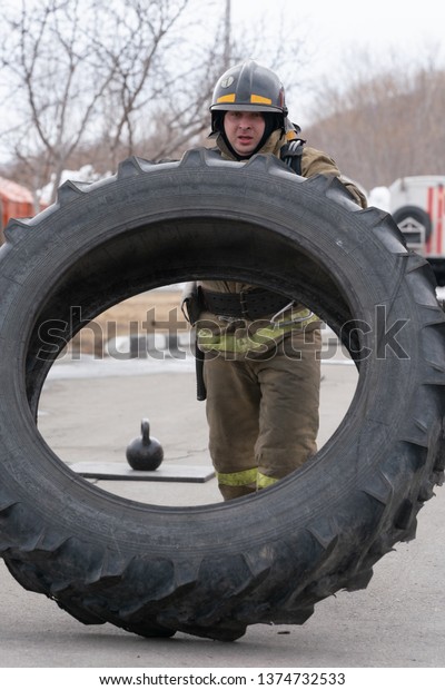 PETROPAVLOVSK CITY, KAMCHATKA PENINSULA,\
RUSSIA - APR 19, 2019: Strong firefighter-rescuer Emercom of Russia\
tilting big tire from truck. Firefighters and rescuers\
(fire-fighting) sport\
competitions.