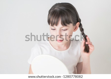Petty girl checking her hair with a hand mirror.