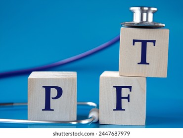 PFT (Pulmonary function test) - acronym on wooden large cubes on blue background with stethoscope