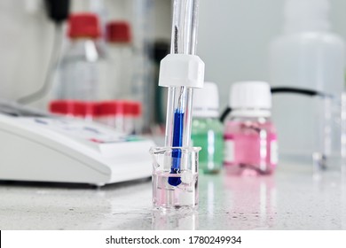 PH Meter With Glass Electrode For Measuring Of Alkalinity And Acidity With Calibration Solution On The Background. Analytical Or Electro Chemistry Laboratory