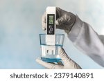 pH meter in hands with gloves, glass of water on a blue background. Measurement of the characteristics of drinking water. The hardness of the water. poor water quality. high values of salt impurities