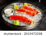 Phalanxes of red crab on ice. Lies on ice with lemon and lime and sauce. Lo key, dark background, horizontal orientation
