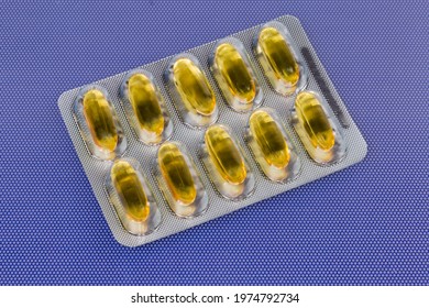 Pharmaceutical Drugs In The Form Of Yellow Translucent Gelatin Capsules In The Blister Packing On A Blue Surface
