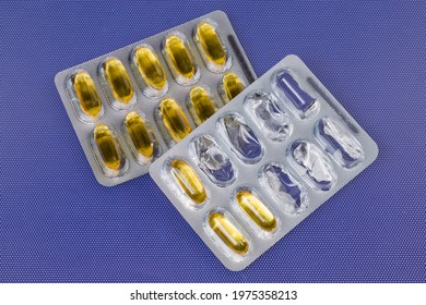 Pharmaceutical Drugs In The Form Of Yellow Translucent Gelatin Capsules In One Started And In One Whole Blister Packing On A Blue Surface, Top View
