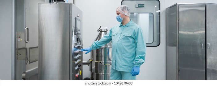 Pharmaceutical factory man worker in protective clothing working with control panel in sterile working conditions