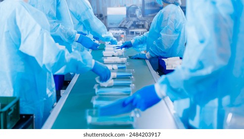 Pharmaceutical factory for production of medical instruments. Worker in uniform working with sterile kit surgical on conveyor belt. - Powered by Shutterstock