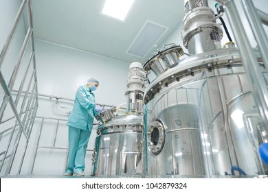 Pharmaceutical factory woman worker in protective clothing operating production line in sterile environment
