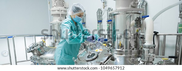 Pharmaceutical factory woman\
worker in protective clothing operating production line in sterile\
environment