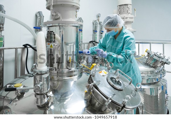 Pharmaceutical factory woman\
worker in protective clothing operating production line in sterile\
environment