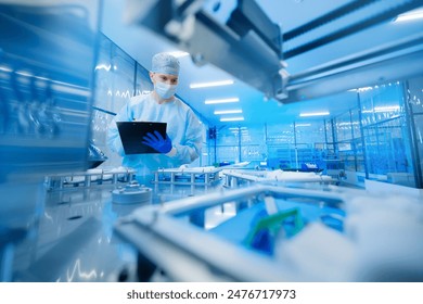 Pharmaceutical factory worker operating production line at pharmacy industry, man use clipboard for control quality. Blue light toning, manufacturing surgery kit box. - Powered by Shutterstock