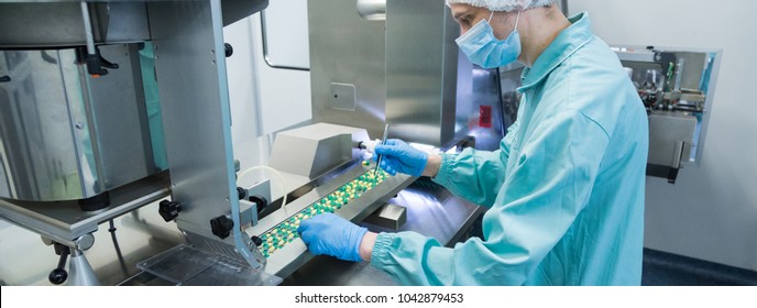 Pharmaceutical industry man worker in protective clothing operating production of tablets in sterile working conditions - Shutterstock ID 1042879453