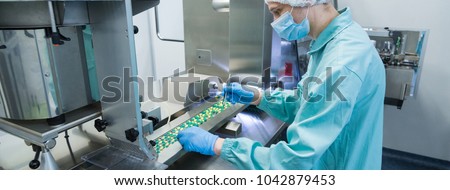 Pharmaceutical industry man worker in protective clothing operating production of tablets in sterile working conditions