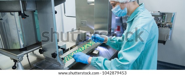 Pharmaceutical\
industry man worker in protective clothing operating production of\
tablets in sterile working\
conditions