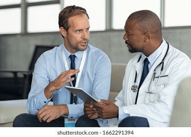 Pharmaceutical representative talking with doctor. African mature practitioner discussing results of the analysis with specialist while consulting diagnosis on digital tablet in hospital room.