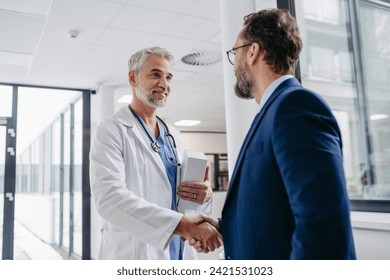 Pharmaceutical sales representative presenting new medication to doctor in medical building, shaking hands.