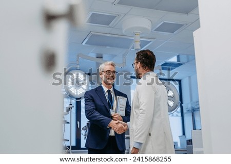 Pharmaceutical sales representative presenting new medication to doctor in medical building, shaking hands. Through door.