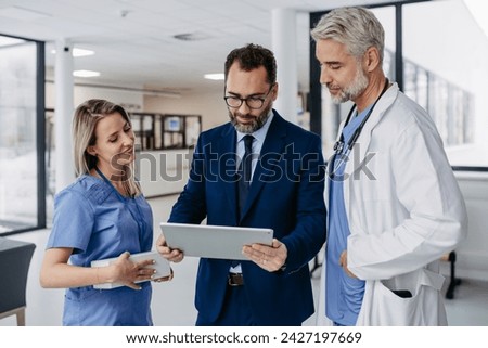 Pharmaceutical sales representative presenting new medication to doctors in medical building, showing on tablet.