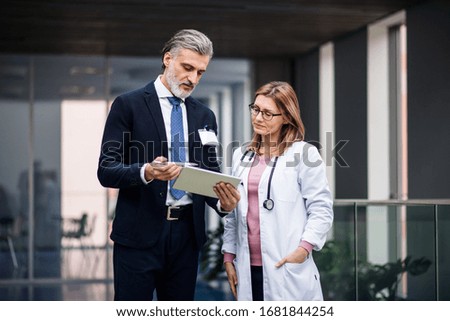 Pharmaceutical sales representative with tablet talking to doctor.