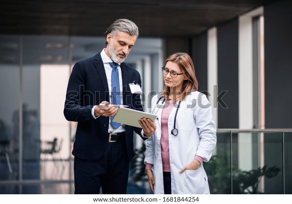Pharmaceutical sales representative with tablet\
talking to\
doctor.