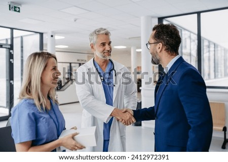 Pharmaceutical sales representative talking with doctors in medical building, shaking hands. Presenting new pharmaceutical product, drugs, medication.