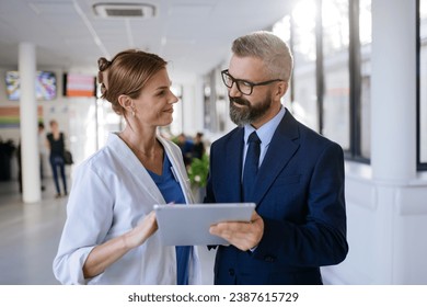 Pharmaceutical sales representative talking with female doctor in medical building. Hospital director consulting with healthcare staff. - Powered by Shutterstock