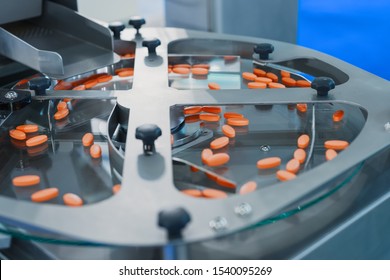 Pharmaceutical Tablet Manufacturing Machine. Orange Pills Are Sorted On A Metal Round Conveyor.