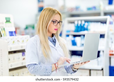 Pharmacist Chemist Woman Standing In Pharmacy Drugstore And Using Laptop For Network Social Media
